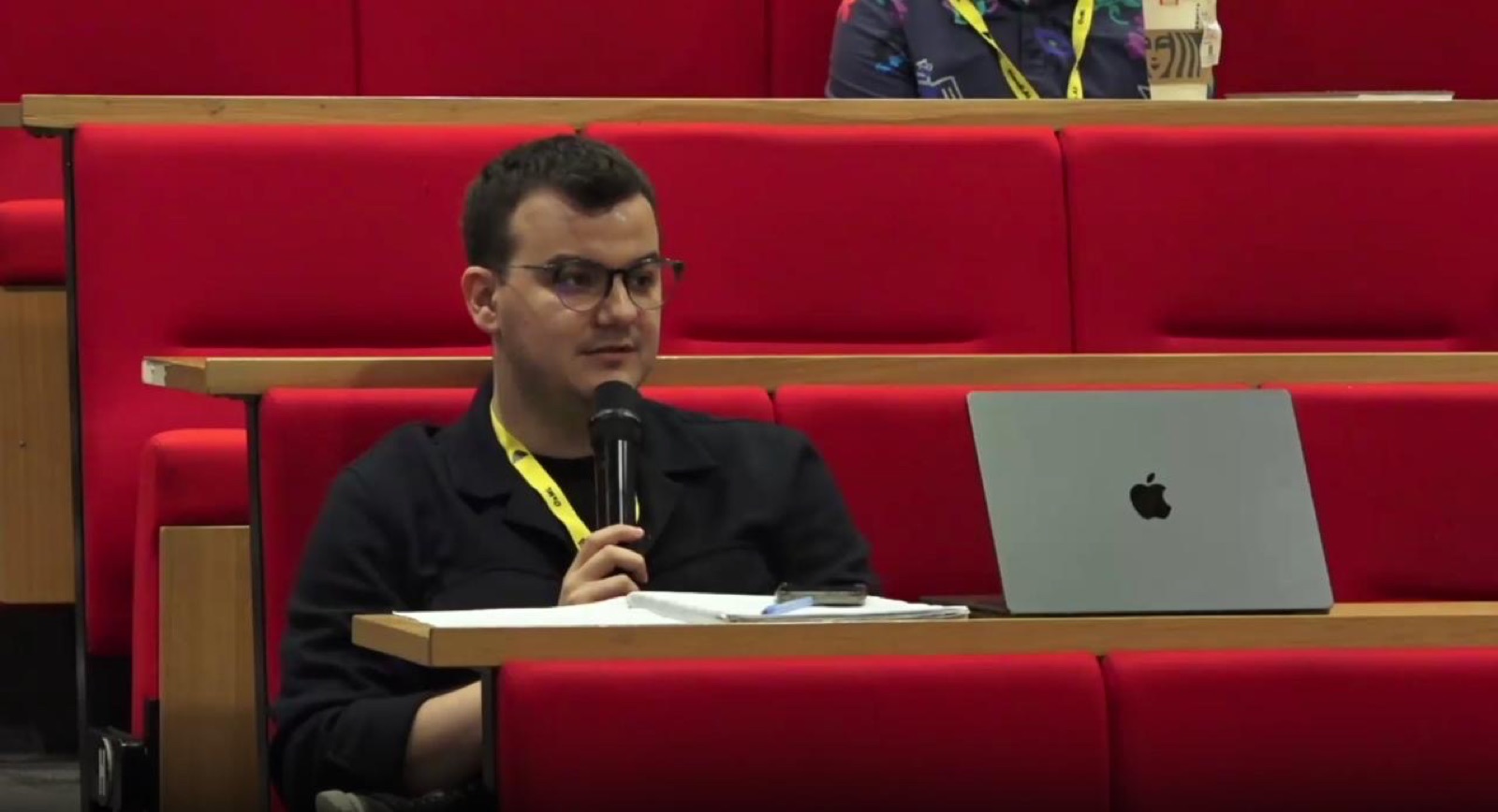Speaking with a microphone from the audience at the Oxford Machine Learning Summer School, 2025