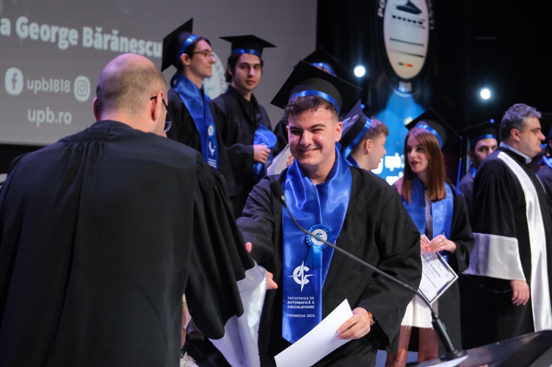 Receiving a diploma on stage, wearing a Faculty of Automatic Control and Computers graduation sash